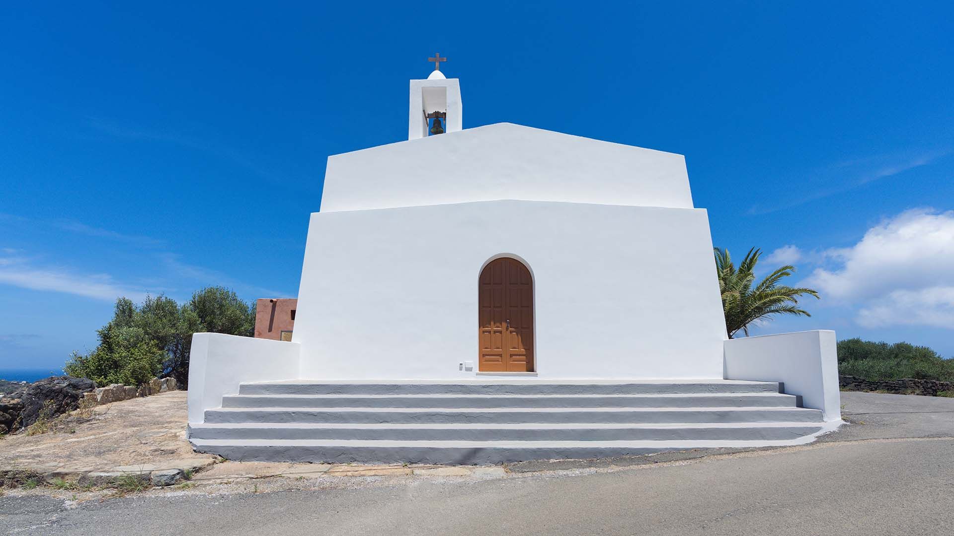 Facciata geometrica bianca della chiesa di Santa Chiara, con gradoni simmetrici e porta centrale ad arco, sormontata da una campana e una croce.