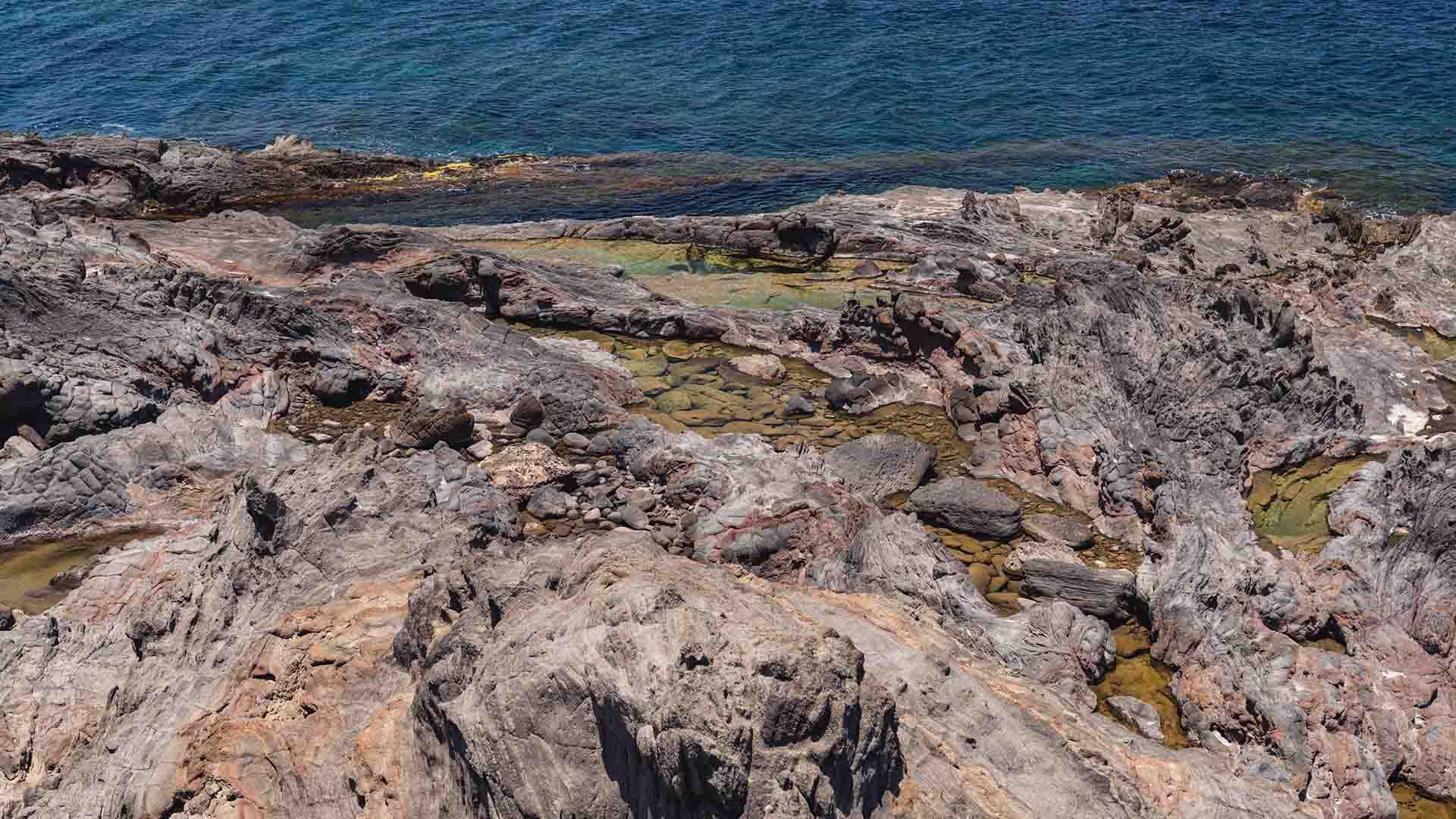 Zona costiera rocciosa della località Gattara a Pantelleria, con formazioni vulcaniche frastagliate e piccole pozze d'acqua trasparente tra le rocce. Sullo sfondo, il mare blu profondo che si estende fino all’orizzonte.