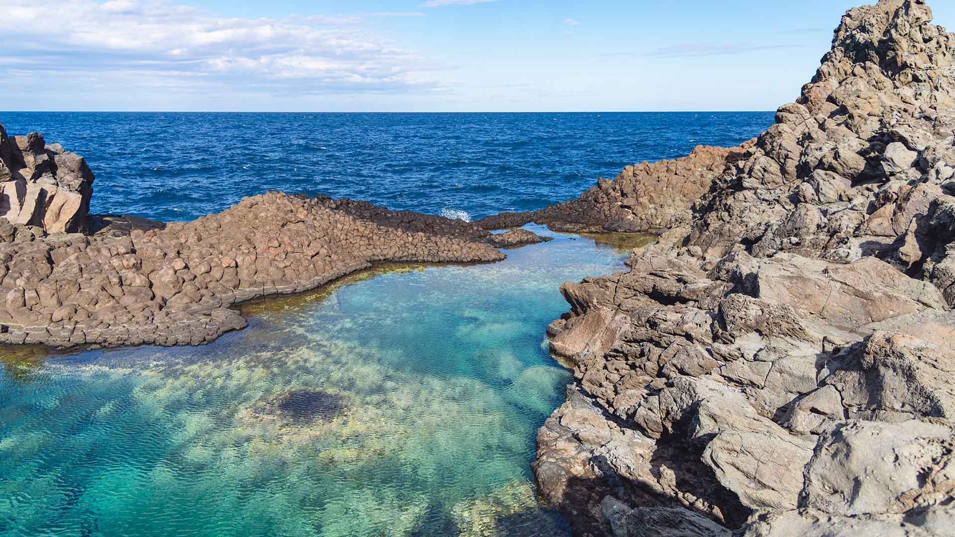 Piccolo specchio d’acqua cristallina racchiuso tra scogli scuri di origine vulcanica, affacciato su un mare blu intenso. Le rocce formano una naturale piscina protetta dalle onde, creando un’oasi tranquilla e suggestiva lungo la costa aspra di Pantelleria