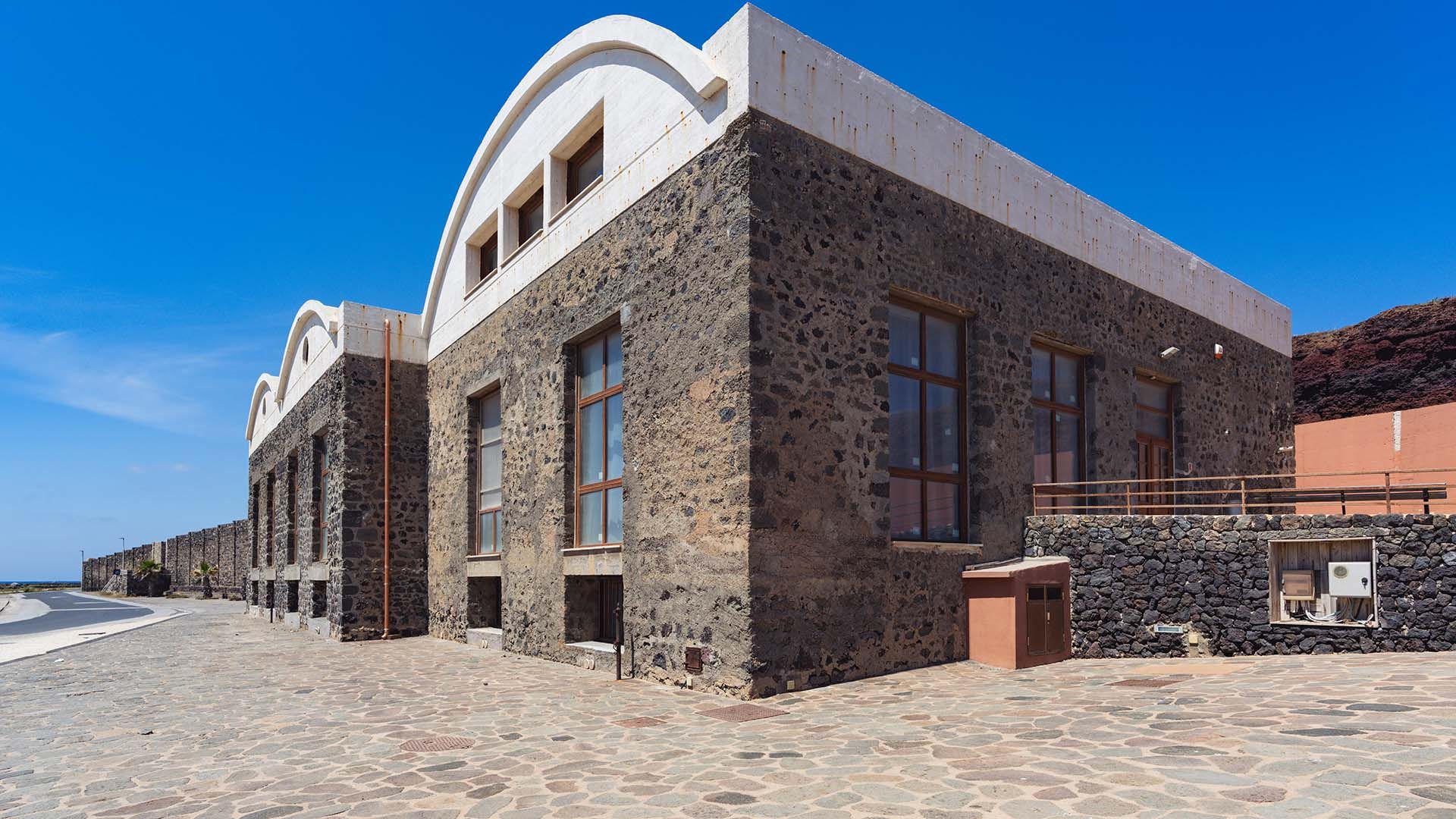 Edificio in pietra lavica con grandi finestre e tetti bianchi arcuati, sede del Museo del Mare di Pantelleria. La struttura si affaccia su una strada lastricata, con vista aperta verso il mare e cielo sereno sullo sfondo.