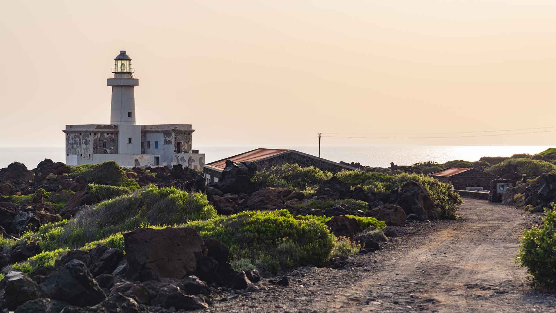 Il Faro di Punta Spadillo a Pantelleria, una torre bianca su rocce laviche con un cielo azzurro intenso.