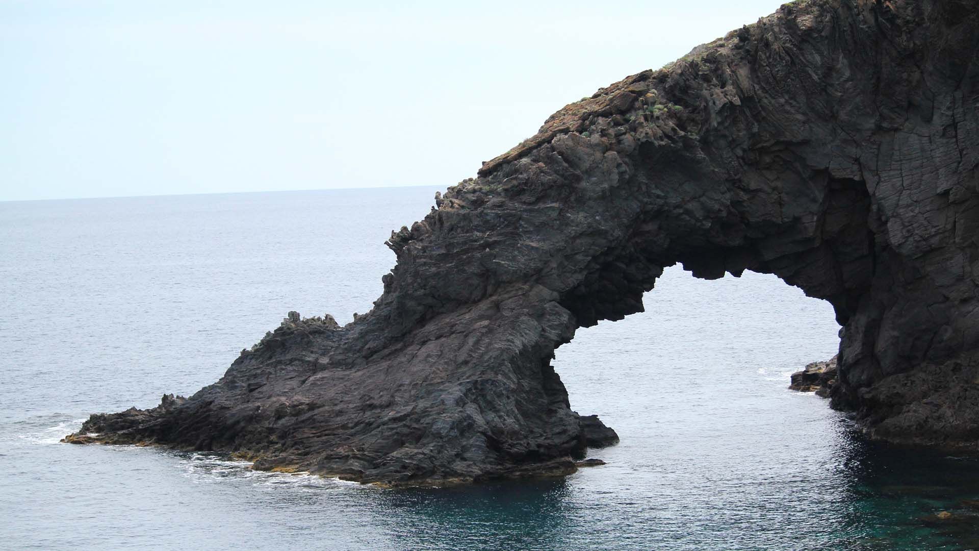L'Arco dell'Elefante, iconica formazione rocciosa lavica di Pantelleria che si erge sul mare blu sotto un cielo sereno.