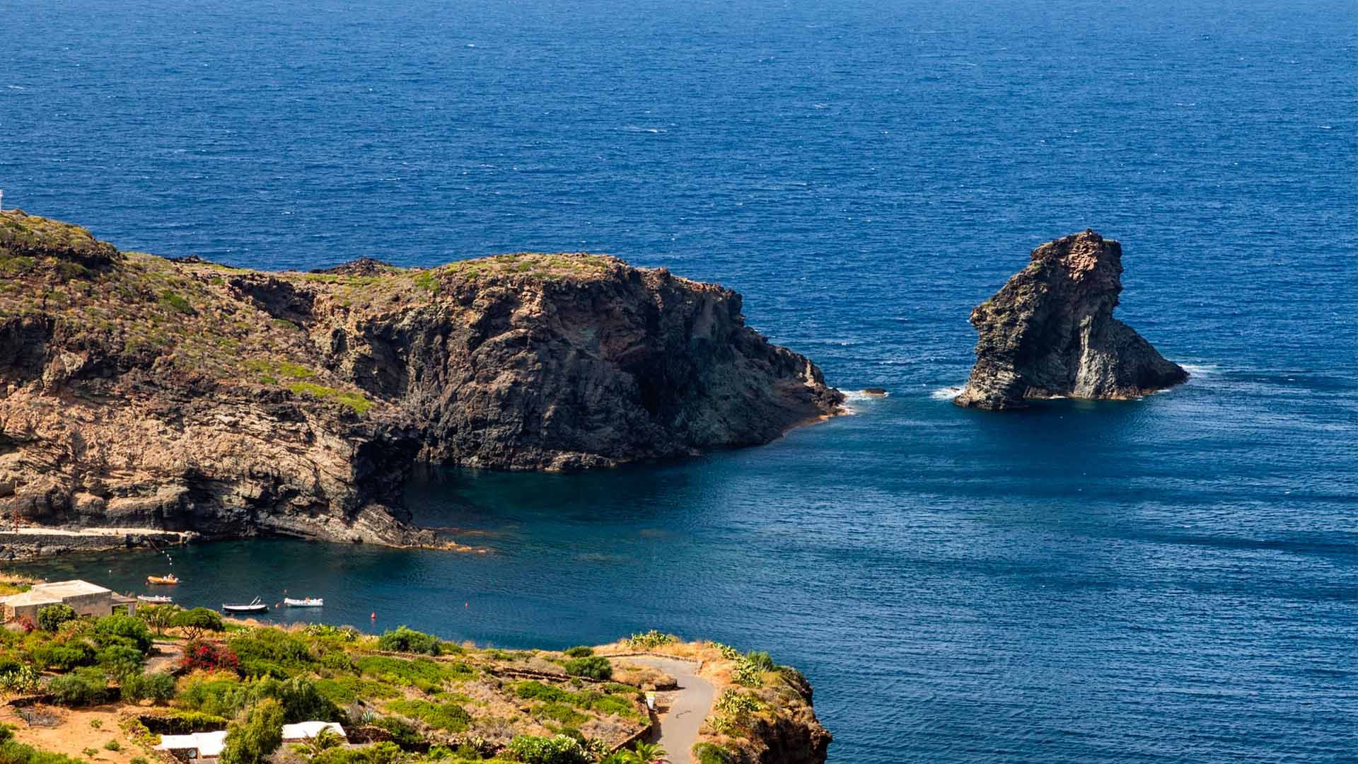 Veduta panoramica della costa rocciosa di Pantelleria con il Faraglione che emerge dal mare blu intenso.