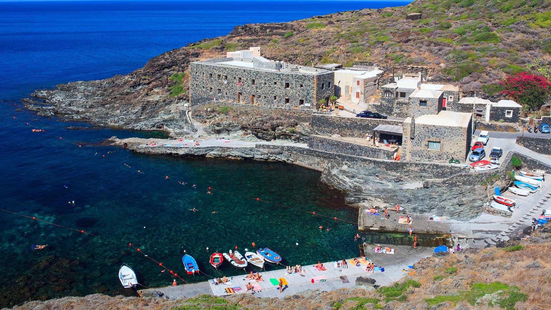 Cala Tramontana a Pantelleria con le sue acque cristalline, le case in pietra lavica e le persone che nuotano e prendono il sole.
