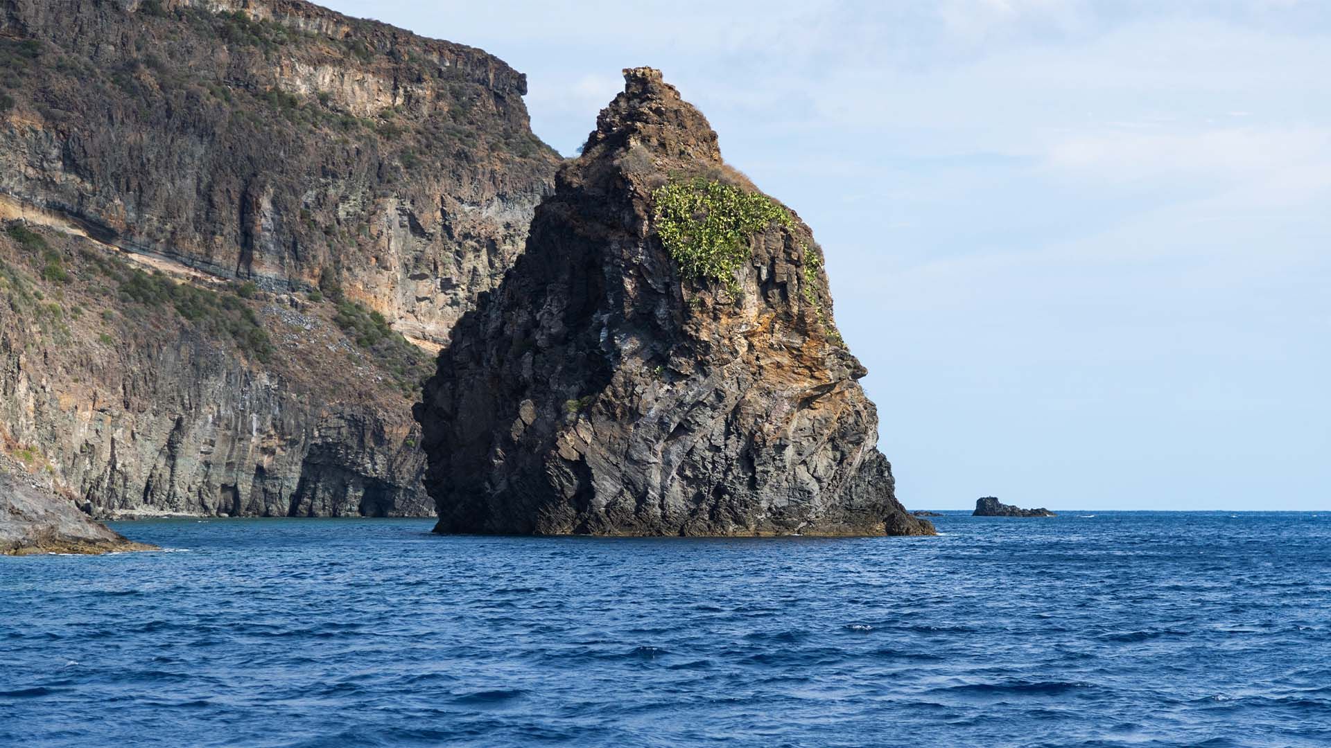 Il Faraglione di Tracino, imponente scoglio vulcanico che emerge dal mare blu di Pantelleria, con scogliere sullo sfondo.