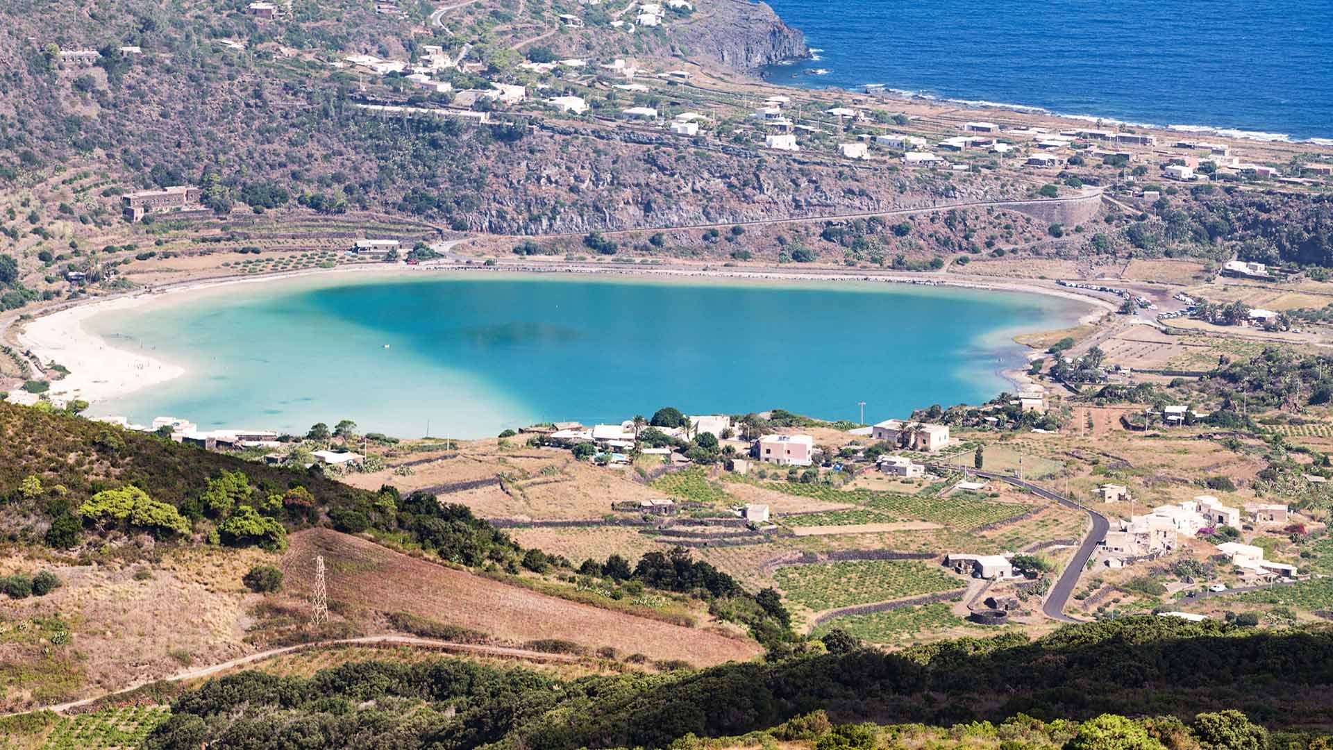 Vista aerea del Lago di Venere (Specchio di Venere) a Pantelleria, circondato da vegetazione, case e la costa rocciosa.