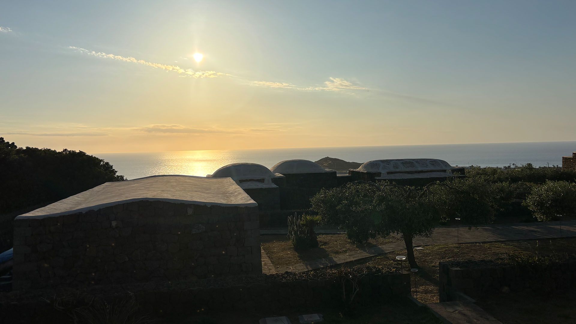 Alba luminosa sul mare di Pantelleria con i caratteristici dammusi e la costa frastagliata in controluce.