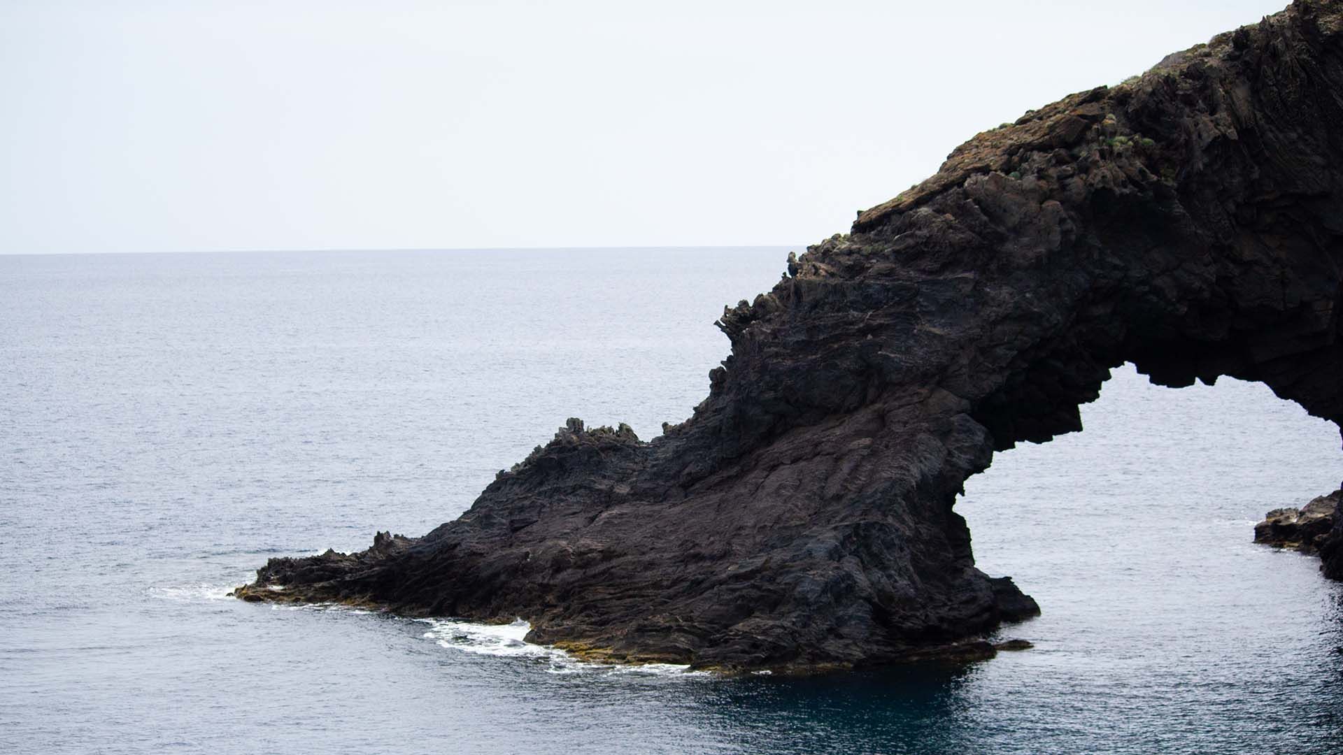 L'Arco dell'Elefante, iconica formazione rocciosa lavica a Pantelleria che emerge dal mare blu sotto un cielo grigio.