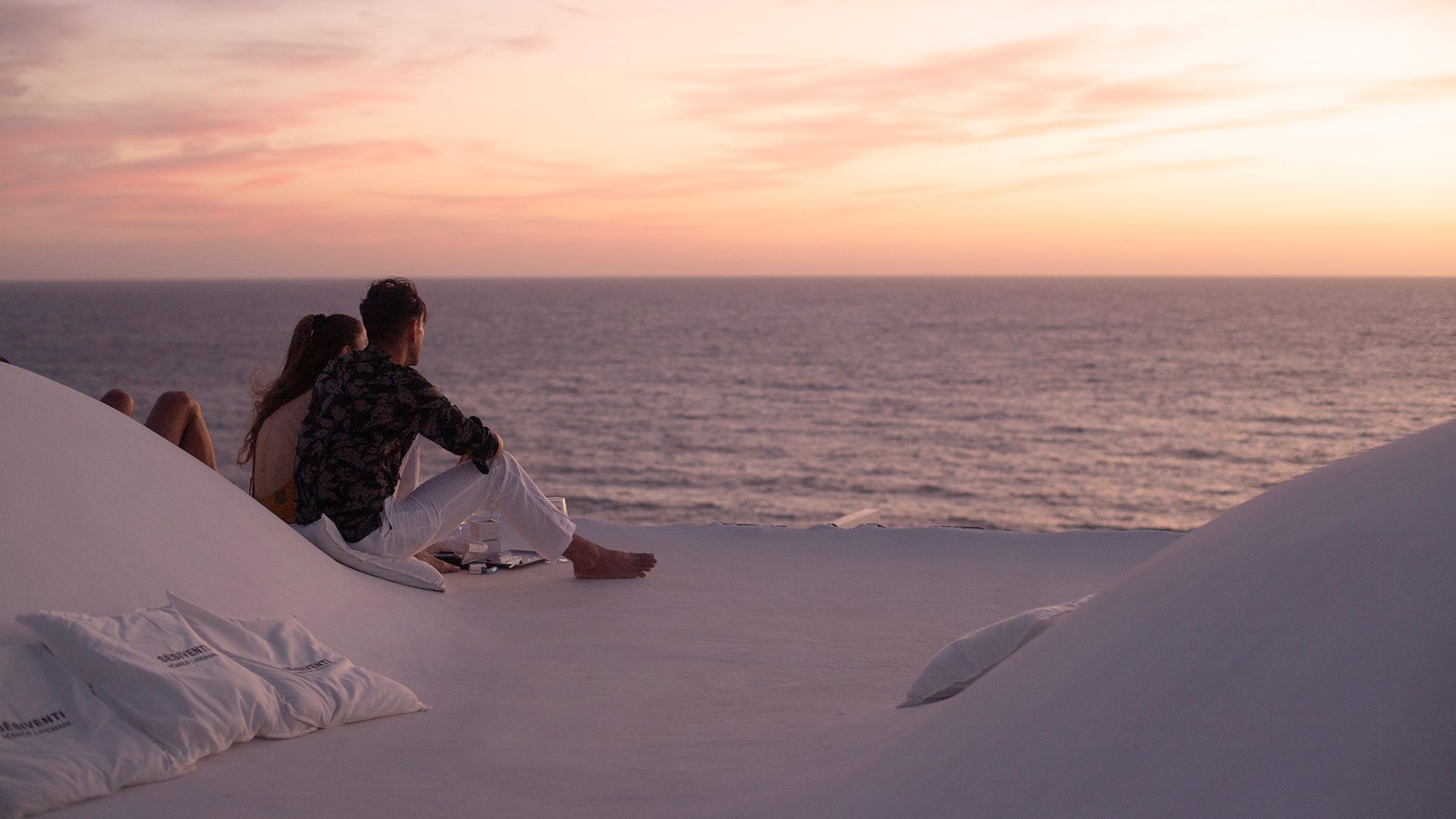 Coppia seduta su una terrazza bianca fronte mare, mentre ammira il tramonto romantico sull'oceano a Pantelleria.
