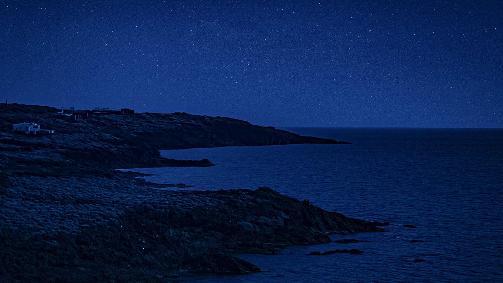 Coste vulcaniche di Pantelleria al chiaro di luna con il mare calmo e il cielo stellato all’orizzonte